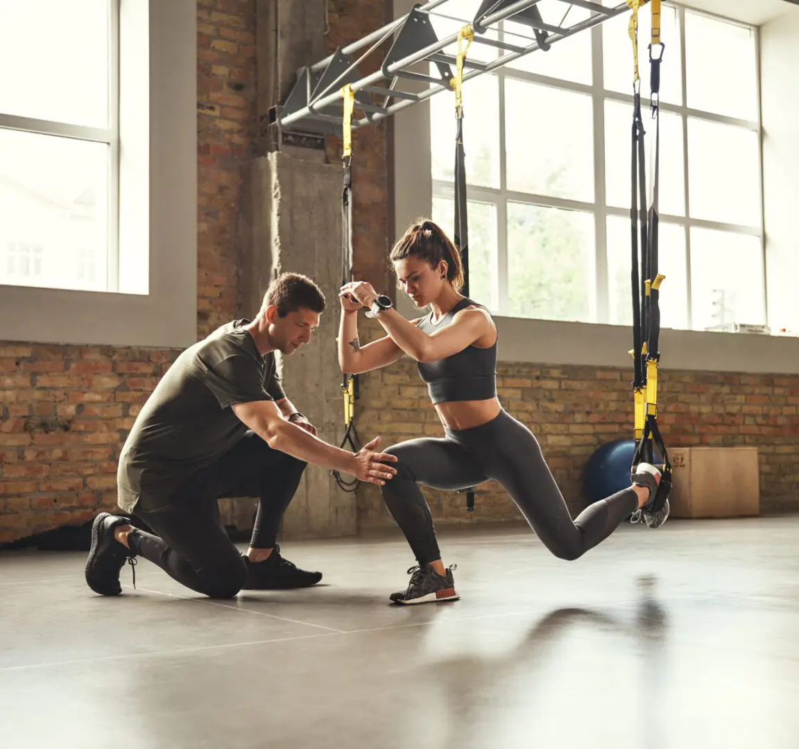 Trainer assisting woman with TRX workout.