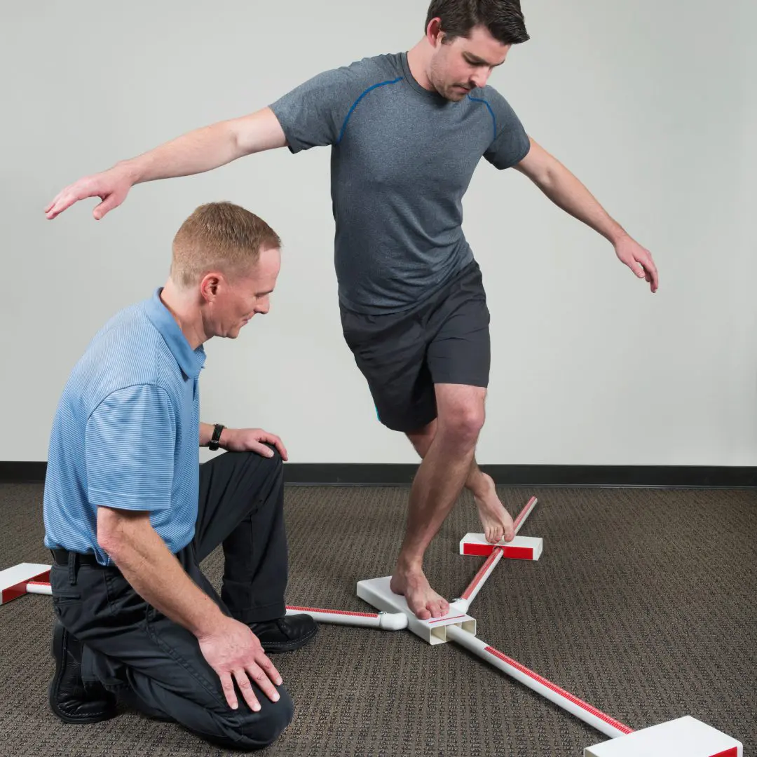 Man balancing on beam with trainer's assistance.
