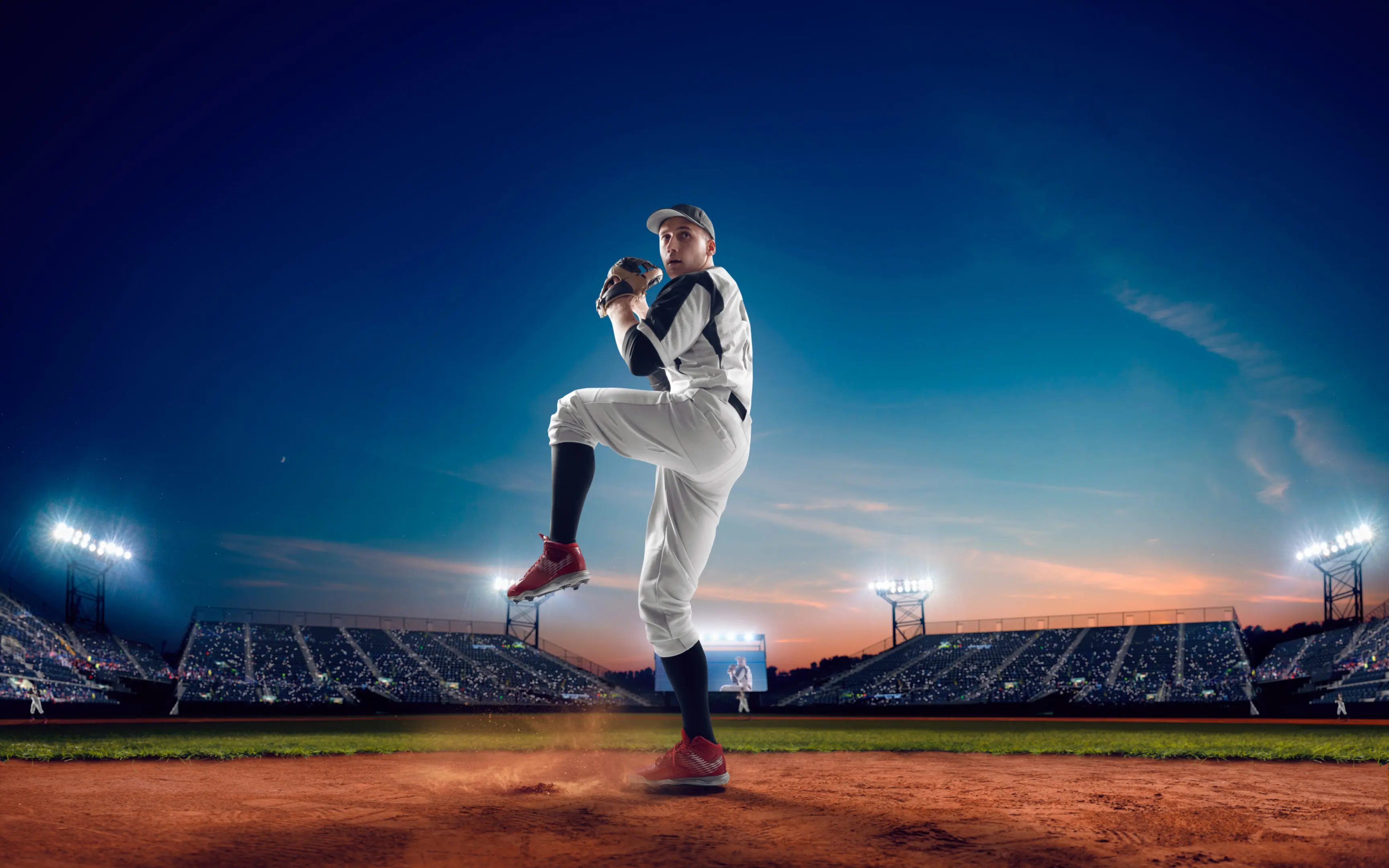 Baseball pitcher prepares to throw a pitch on a brightly lit field at dusk.