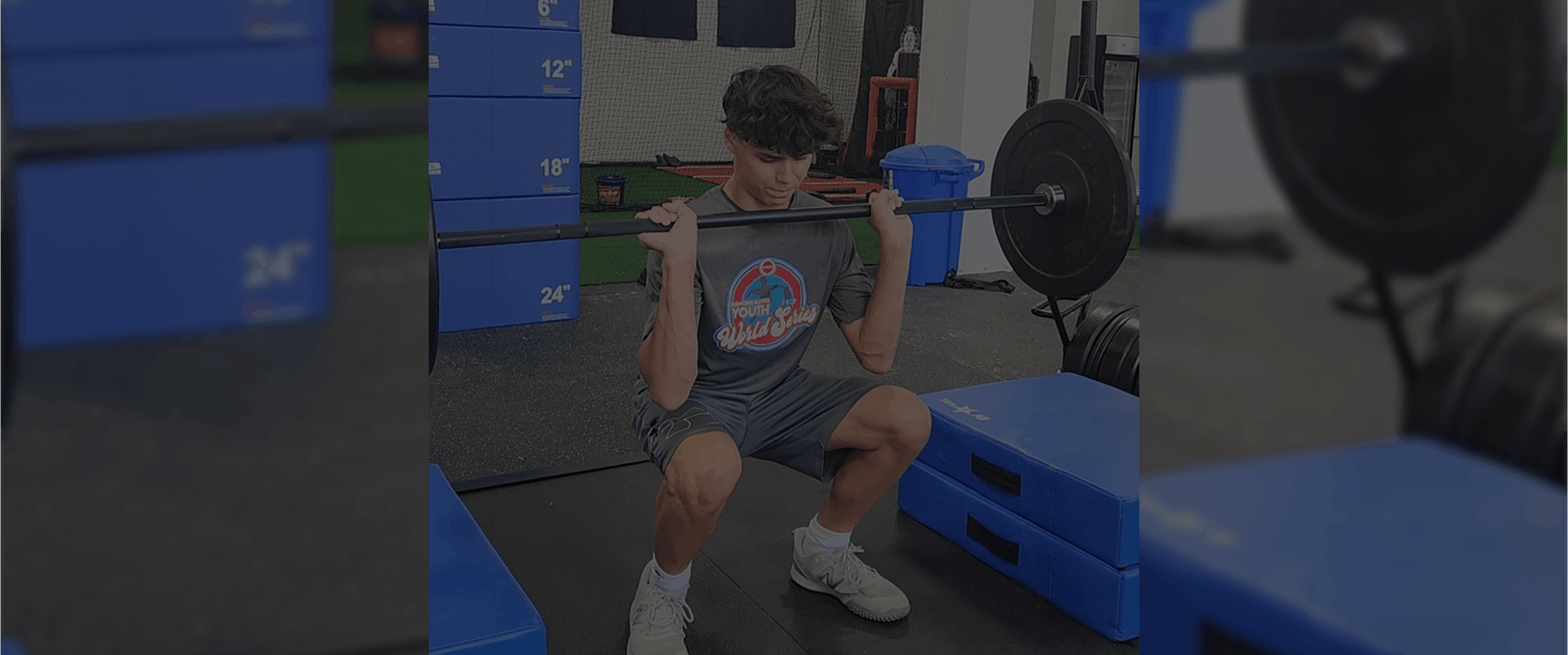 A young man squats while lifting a barbell in a gym setting.