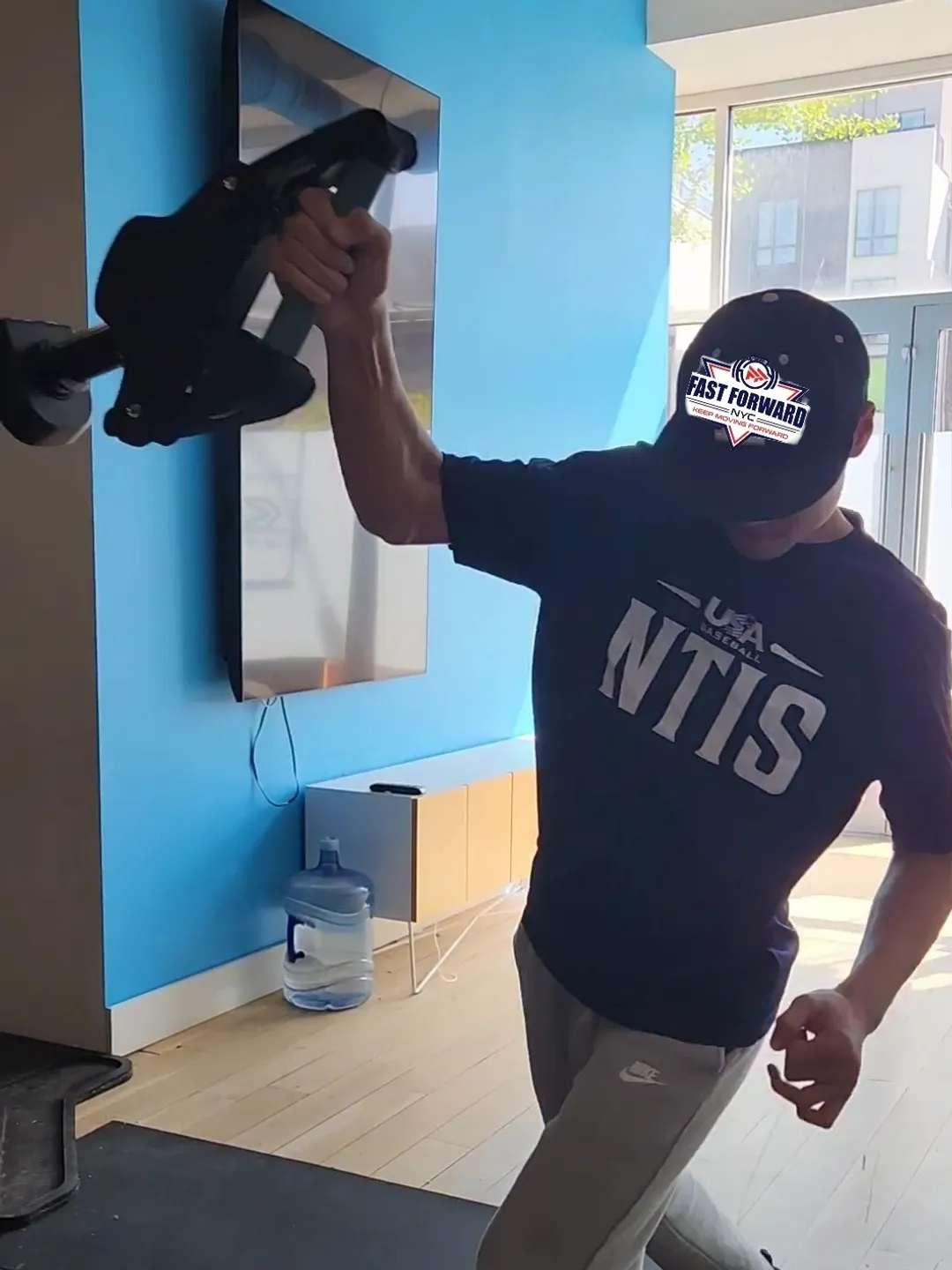 Person wearing an NTIS shirt and cap indoors.
