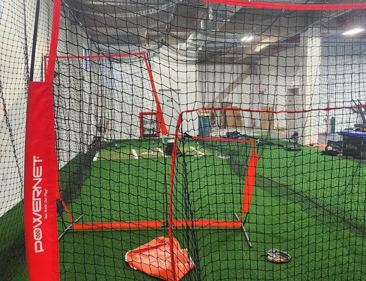 Indoor sports training area with pitching nets and green turf.