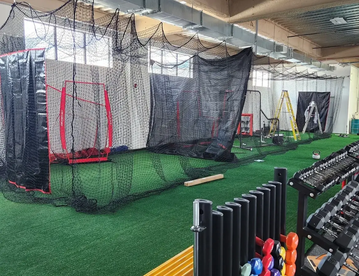Indoor baseball training facility with pitching nets and equipment.