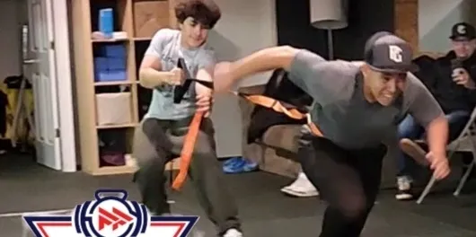 Two boys playing tug-of-war with an orange strap inside a room.