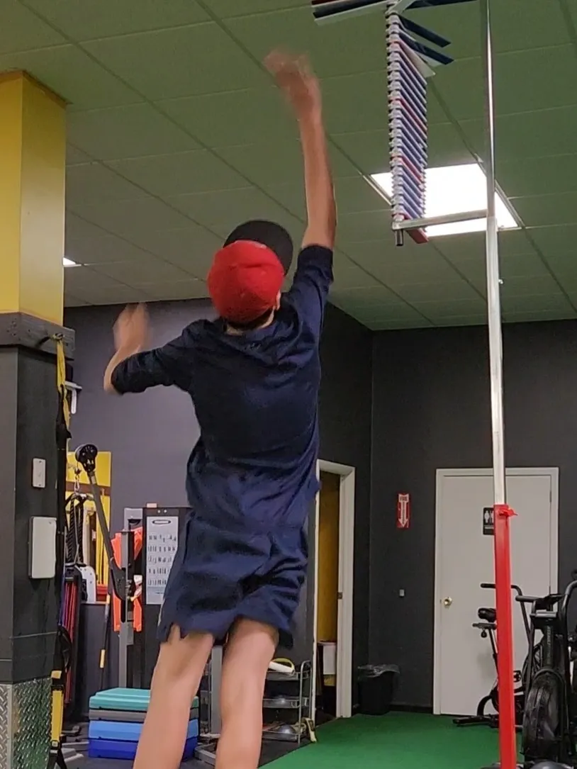 Person in red cap jumping to grab a bar in a gym.